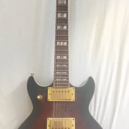 Elektrická kytara s tmavým, přechodovým povrchem od černé po hnědou a zlatými komponenty. Na hlavě je bílý nápis Ibanez a logo s ornamentem, hриф má…