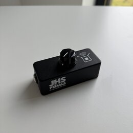 Černý efekt pedál obdélníkového tvaru s jedním ovládacím knoflíkem. Na boku je bílý nápis JHS PEDALS a pod ním menší text LITTLE BLACK AMP BOX. V hor…
