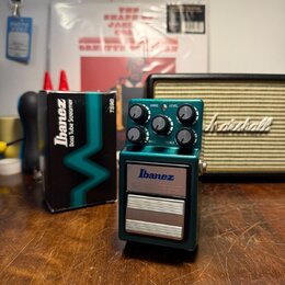 Kytarový efekt v zeleném kovovém krytu s nápisy Ibanez, TS9B a Bass Tube Screamer. Na horní části jsou čtyři ovládací knoflíky s popisky DRIVE, LEVEL…