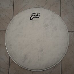 Bílá kruhová bubenová kože v kovovém obruči. Na pravé straně je černé logo s nápisy „Evans“ a „'56“ a menším textem „CRAFTED IN USA“. Povrch kože vyk…
