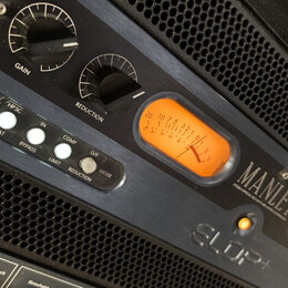 Detailní pohled na rackové studio zařízení značky MANLEY. Na čelním panelu jsou dva analogové VU metry s oranžovým podsvícením, dva otočné ovladače s…