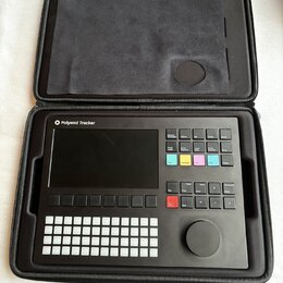 Černý sampler Polyend Tracker v černém přepravním pouzdře. Zařízení má displej, mřížku bílých tlačítek a několik barevných ovládacích prvků s nápisy…