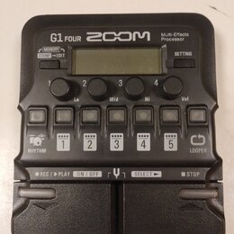 Černý multi-efektový procesor s nápisy G1 FOUR, ZOOM a Multi-Effects Processor. Zařízení obsahuje displej, čtyři otočné ovladače s popisky Lo, Mid, H…