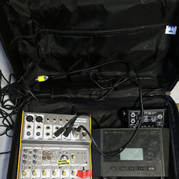 Černý přenosný kufr s elektronickým vybavením. Uvnitř jsou dva mixážní pulty značky TAPCO, z nichuž horní nese nápis MIX 600. Na spodním mixážním pul…