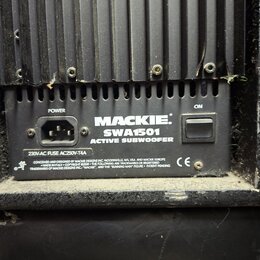 Detail zadní strany černého aktivního subwooferu. Na přístrojovém panelu je nápis MACKIE SWA1501 ACTIVE SUBWOOFER, napájecí konektor označený jako PO…