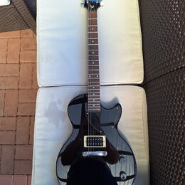 Černá elektrická kytara s tmavým hnedým hmatníkem a černým pickguardem. Na hlavě je bílý nápis Epiphone. Nástroj vykazuje známky běžného používání, p…