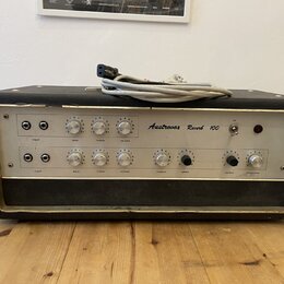 Černý kytarový kombozesilovač s bílým předním panelem a kovovým rámem. Na panelu je nápis Austrovox Reverb 100 a řada ovládacích knoflíků s popisky i…