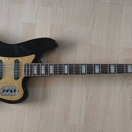 Černá elektrická kytara s hnědým hmatníkem a zlatavým pickguardem. Na hlavě nástroje je nápis Squier II. Kytara má tři snímače typu single-coil a chr…