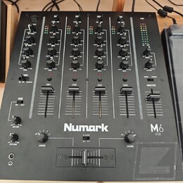 Černý mixážní pult s nápisem Numark a označením M6 USB. Zařízení obsahuje čtyři vstupní kanály (CH1 až CH4) a jeden Master kanál, každý s posuvníkem…