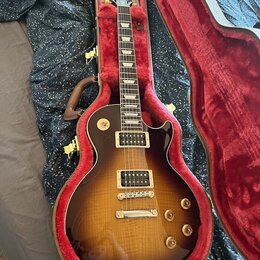 Elektrická kytara s trupem ve tvaru Les Paul v barevné variantě sunburst, umístěná v otevřeném tvrdém kufru s červeným polstrováním. Nástroj má dva h…