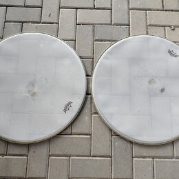Dvě bílé bicí blány s kovovými obručemi položené na dlažbě. Obě blány mají v horní nebo dolní části logo REMO. Povrchy blan vykazují známky opotřeben…