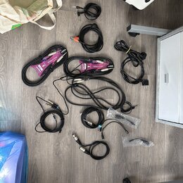 Fotografie zobrazuje sadu různých audio kabelů rozložených na šedé podlaze. Jsou zde černé kabely s různými konektory, včetně dvou kabelů v fialových…