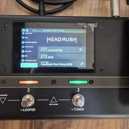 Černý kytarový procesor s displejem a expresním pedálem. Na displeji je nápis HEADRUSH, verze softwaru V 5.1.0 (2A63755), hardware B (10.065) a název…