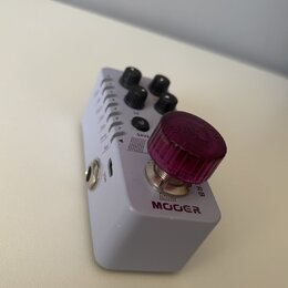 Bílý kytarový pedál značky MOOER s fialovým plastovým knoflíkem, na kterém je nápis SWEEPER. Na horní části jsou čtyři černé oválné knoflíky a tlačít…
