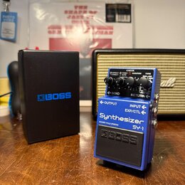 Modrý kytarový pedál s nápisy Synthesizer, SY-1 a BOSS. Na horním ovládacím panelu jsou dva černé knoflíky, červená kontrolka CHECK a přepínače EFFEC…