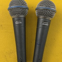 Dvě dynamické mikrofony s kovovými mřížkami a šedými trupy. Na obou je viditelný štítek s nápisem SHURE BETA 58A. Povrch trupů vykazuje drobné známky…