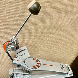Stříbrný bubnový pedál s logem Pearl na základně a na beateru. Na pedálu je připevněna bílá visačka s nápisy DRUM PEDAL a MODEL NO. P-930. Povrch ped…