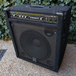 Černý basový kombozesilovač s látkovým potahem a kovovou mřížkou před reproduktorem. Na horním ovládacím panelu je nápis Beta Alvin a BASS AMPLIFIER…