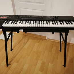 Černý digitální klavír umístěný na černém X-stojanu. Na levé straně korpusu je bílý nápis Roland a pod ním modelové označení Juno-D, doplněný červený…
