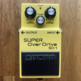 Žlutý efekt pedál s černým spínacím tlačítkem. Na spodní části je nápis SUPER Over Drive SD-1 a na spínači logo BOSS. V horní části jsou tři ovládací…