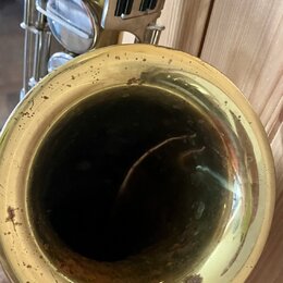Detailní pohled na čňel mosazného saxofonu. Povrch uvnitř i vně čněle vykazuje výrazné známky opotřebení, oxidaci a tmavé skvrny. V horní části je vi…