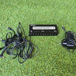 Černý napájecí zdroj pro efektové pedály s bílým nápisem POWER SUPPLY 2 a logem JOYO. Zařízení má v dolní části řadu výstupů pro konektory. K zdroji…