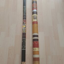 Dvě didgeridou z dřeva s různým povrchovým zdobením. Levý nástroj je tmavě hnědý s barevnými ornamenty a vzory. Pravý nástroj je světlejší, zdobený h…