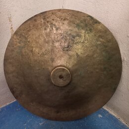 Kruhový mosazný činel s vyvýšeným středem. Povrch je výrazně opotřebovaný, s viditelnými škrábanci a tmavšími skvrnami oxidace. Na povrchu není žádný…