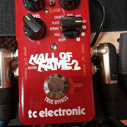 Červený efekt pedál s nápisy HALL OF FAME 2, REVERB a tc electronic. Na horní části jsou čtyři černé ovládací knoflíky s popisky PRE-DELAY, LEVEL a d…