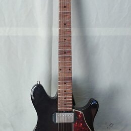 Černá elektrická kytara s tmavě hnědým hnedem hmatníkem a dřevěnou hlavou. Na hlavě je viditelné logo "Cort". Kytara má dva humbuckery, červeně vzoro…