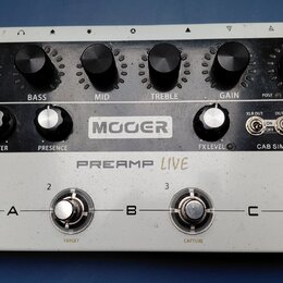 Bílý kytarový předzesilovač značky MOOER s označením PREAMP LIVE. Horní panel obsahuje šest černých otočných ovladačů s popisky VOL, BASS, MID, TREBL…