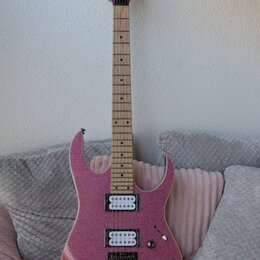 Elektrická kytara s růžovým třpytivým povrchem a světlým hnedým hnedým hmatníkem. Na hlavě je viditelný nápis Danelectro. Nástroj má dva snímače typu…