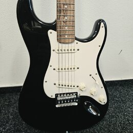 Černá elektrická kytara typu Stratocaster s bílým pickguardem a hnedým hmatníkem. Nástroj má tři snímače s bílými krytkami, jeden volič tónu a dva po…