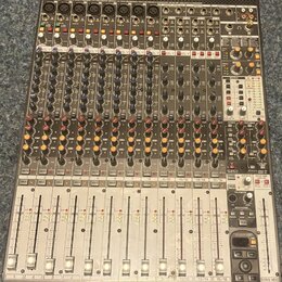Šedý mixovací pult s mnoha ovládacími prvky, posuvníky a konektory. V horní části je nápis Behringer XENYX UFX1604. Povrch přístroje vykazuje mírné z…