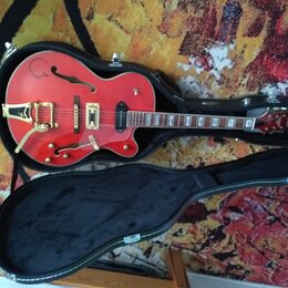 Červená polodupová elektrická kytara v černém tvrdém kufru. Na horní dece je vidět nápis "Epiphone" na hlavě hmatníku a zlatý hardware. Povrch nástro…