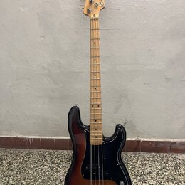 Elektrická basová kytara s trupem v sunburst provedení a černým pickguardem. Na hlavě hmatníku je viditelný nápis Squier. Krk a hmatník jsou vyrobeny…