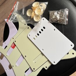 Sada dílů pro elektrokitaru v různých odstínech bílé a krémové. Soubor obsahuje tři plechy (pickguardy), plastové knofíky v sáčku a kovové šroubky v…