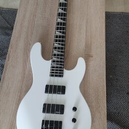 Bílá elektrická basová kytara s černým hmatníkem a černými komponenty. Na obou snímačů je viditelný nápis "schecter". Nástroj má tři ovládací knofíky…