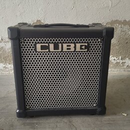 Černý kytarový kombozesilovač s kovovou mřížkou reproduktoru. Na horní části mřížky je bílý nápis CUBE. Nástroj má v horní části přenosnou rukojeť a…