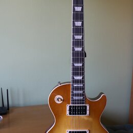 Elektrická kytara s trupem v žlutém gradientu (sunburst) a tmavým hmatníkem s trapezoidními vložkami. Na hlavě je bílý nápis Gibson. Nástroj má dva h…