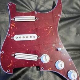 Vinylový pickguard v tmavě červené barvě s texturou želvy, osazený třemi bílými snímači. Na ovládacích knoflících jsou nápisy VOLUME, TOINE a ONE. So…