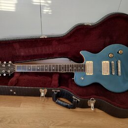 Modře lakovaná elektrická kytara typu Les Paul v černém tvrdém kufru s červeným polstrováním. Na hlavě hmatníku je bílý nápis Summit a text MADE IN K…