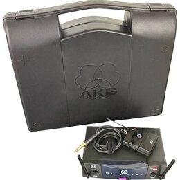 Černý plastový kufřík s vyraženým logem AKG. Před ním je umístěn bezdrátový přijímač s nápisy SR 40 a AKG Wireless System, vysílač s logem AKG a kabe…