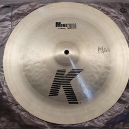 Kruhový činel z kovu s viditelným kování povrchu. Na horní části je nápis MINI CHINA a pod ním 14"/36cm, ve spodní části je velké logo K. V pravé čás…