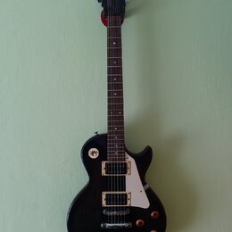 Černá elektrická kytara s tvarem single-cut a bílým pickguardem. Na hlavě hmatníku je bílé logo Epiphone. Nástroj má dva humbuckery s krémovými rámeč…