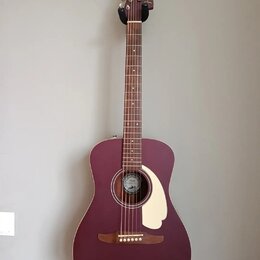 Akustická kytara v matové vínové barvě s krémovým pickguardem. Na hlavě hmatníku je bílý nápis Fender. Uvnitř ozvučovacího otvoru je vidět štítek s l…