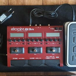 Červený multi-efektový procesor s nápisem ZOOM B3n Multi-Effects Processor. Zařízení má tři displeje, ovládací knoflíky a tři nožní spínače označené…