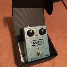 Krytá krabička s efekt pedálem v modro-zelené barvě s texturovaným povrchem. Na pedálu je logo MXR a nápis CLASSIC 108 FUZZ. Jsou zde dva černé ovlád…