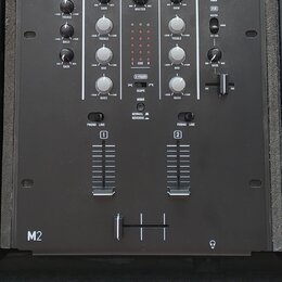 Černý DJ mixér značky Numark s označením M2 v levém dolním rohu. Přístroj obsahuje řadu otočných knoflíků pro ovládání GAIN, TREBLE, MID a BASS, cent…