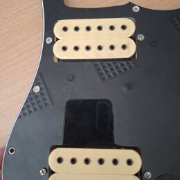 Černý plastový pickguard s dvěma humbuckery v krémové barvě. Snímače mají viditelné černé póly a jsou přišroubované k desce. Na povrchu pickguardu js…